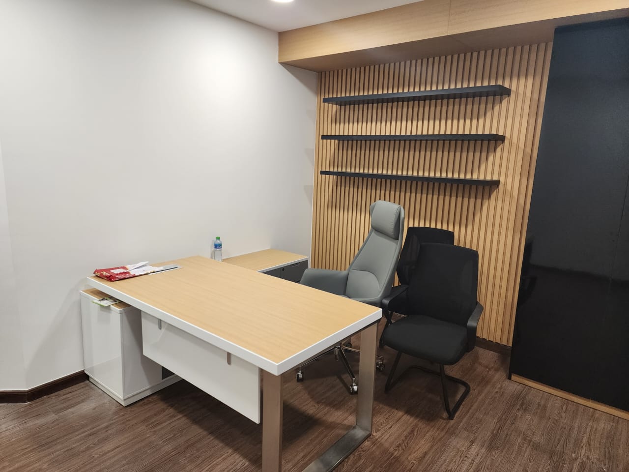 Modern office interior: Open-plan layout, white walls, exposed brickwork, dark wood flooring, black ceiling. Sleek gray workstations, ergonomic chairs, comfy sofas, greenery. Bright, inviting atmosphere. Stylish black-and-white reception counter.